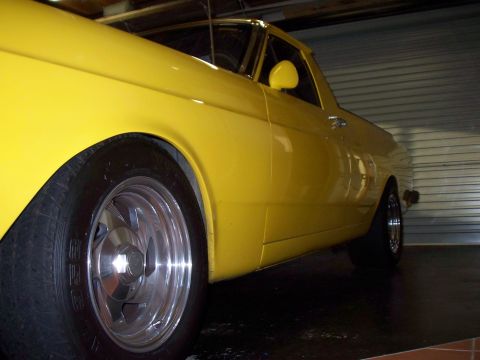 1985 Ford Bronco - A yellow pickup truck with custom wheels is parked inside a garage.