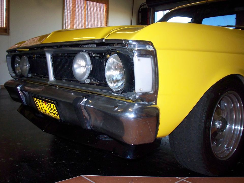 Yellow car front end with chrome bumper and grille. License plate reads NTC-066