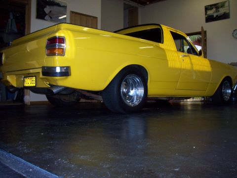 1985 Ford Bronco - A yellow pickup truck is parked indoors, its rear end with chrome accents and dual exhaust pipes.
