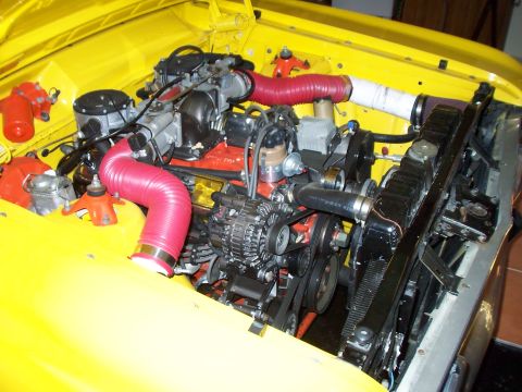 1985 Ford Bronco - The engine bay of a yellow vehicle features red intake hoses and a black radiator, with a Supermotors watermark at the bottom.