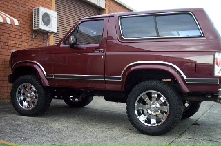 1985 Ford Bronco - This maroon Ford Bronco, likely from the early 1980s, is shown from its side profile with custom chrome wheels.