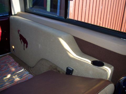 1985 Ford Bronco - The side panel of a vehicle's interior features a red bronco graphic and a cup holder.