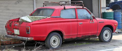 1972 Ford Ranchero - This weathered red pickup truck sits with flat tires, showing significant rust and a tarp covering its bed.