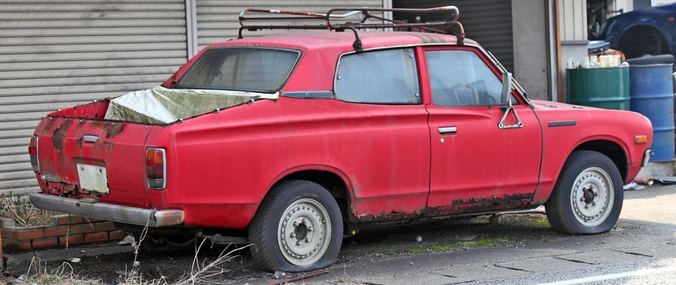 red pickup truck with flat tires and a roof rack parked outside a garage