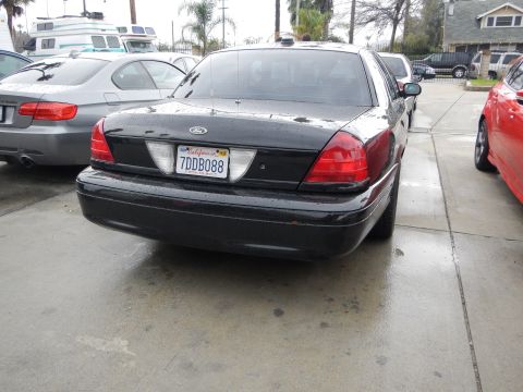 2003 Ford Crown Victoria - Rear three-quarter view of a black Ford Crown Victoria sedan with California plate 7DDB088, parked on rain-soaked pavement.