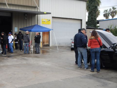 2003 Ford Crown Victoria - group of people, including some near a black car with an open hood, gathers outside an auto shop under a blue tent and Pacesetter banner.