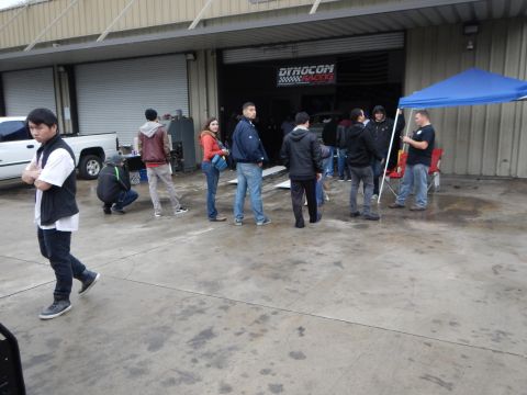 2003 Ford Crown Victoria - group of people stands on the concrete outside an open auto shop bay marked with a Dynocom Racing banner.
