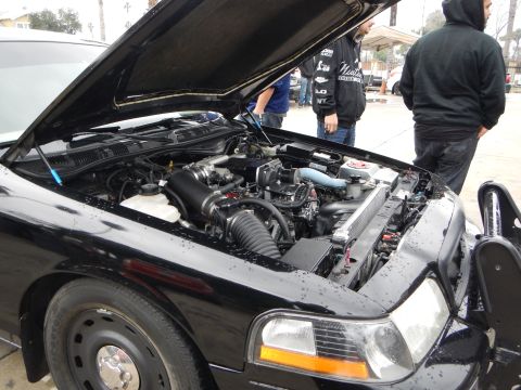 2003 Ford Crown Victoria - open hood of a black car reveals its engine bay with intake plumbing and a radiator, as two people stand behind it.