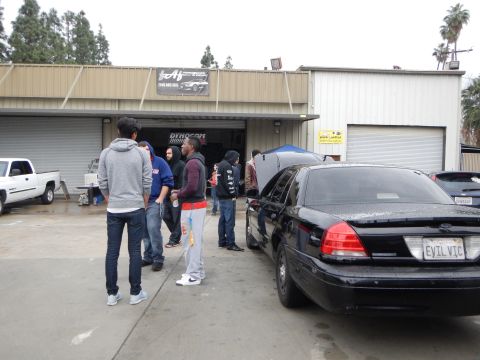 2003 Ford Crown Victoria - black Ford Crown Victoria with an 'EVIL VIC' personalized plate is parked outside an auto shop as young men gather nearby.