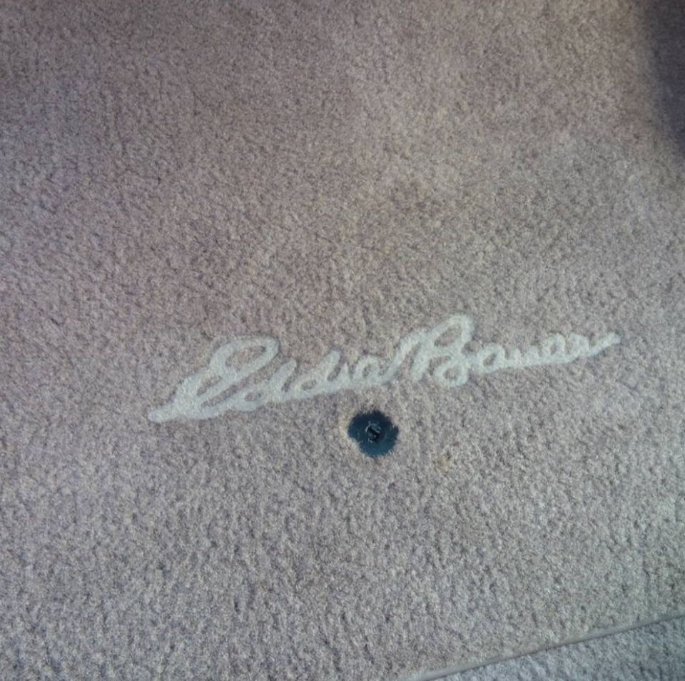 Tan carpet with embroidered Eddie Bauer script logo and a floor mat grommet hole