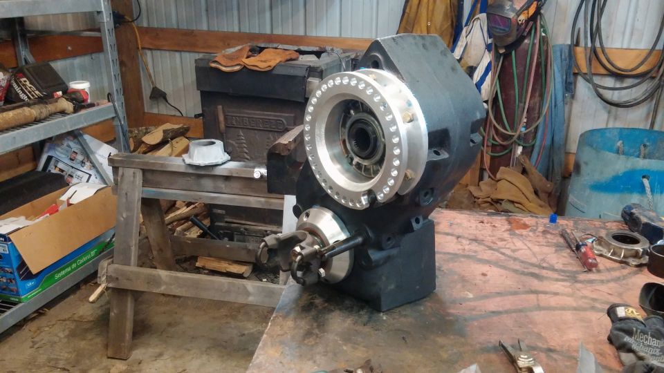 Black transfer case with silver bolted flange, resting on a workbench