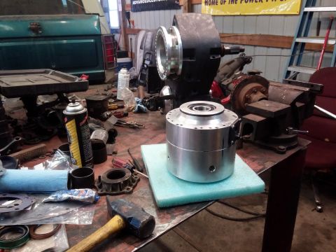 1995 Ford Bronco - A transfer case doubler part sits on a workbench amidst tools and automotive parts, with the rear of a green truck visible.