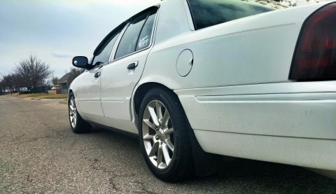 2000 Mercury Grand Marquis - A white 2000 Mercury Grand Marquis sedan is viewed from the side, parked on a street with a cloudy sky above.