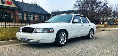 2000 Mercury Grand Marquis - White 2000 Mercury Grand Marquis parked on a street with a building in the background.