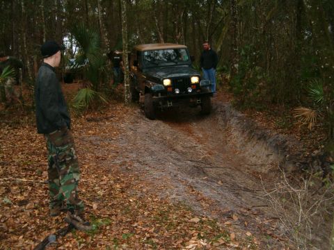 1991 Ford Bronco - A Jeep Wrangler TJ navigates a muddy off-road trail surrounded by trees and fallen leaves.