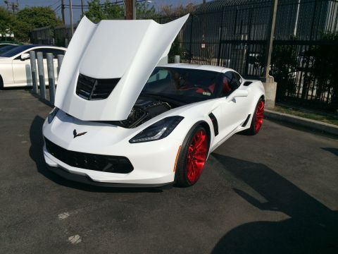 1968 Ford Mustang - White Chevrolet Corvette with hood open, red wheels, parked outdoors.
