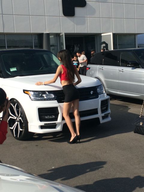 1968 Ford Mustang - A woman poses next to a white Range Rover at an outdoor event with other vehicles present.