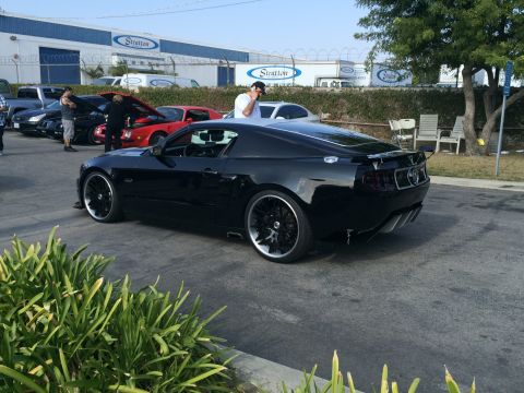 1968 Ford Mustang - A black custom coupe is parked in a lot with other cars and a building in the background.