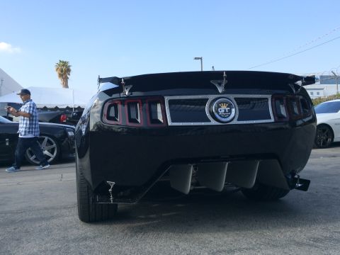 1968 Ford Mustang - A black Ford Mustang with a GT emblem and spoiler is parked outdoors, with other vehicles and a person in the background.