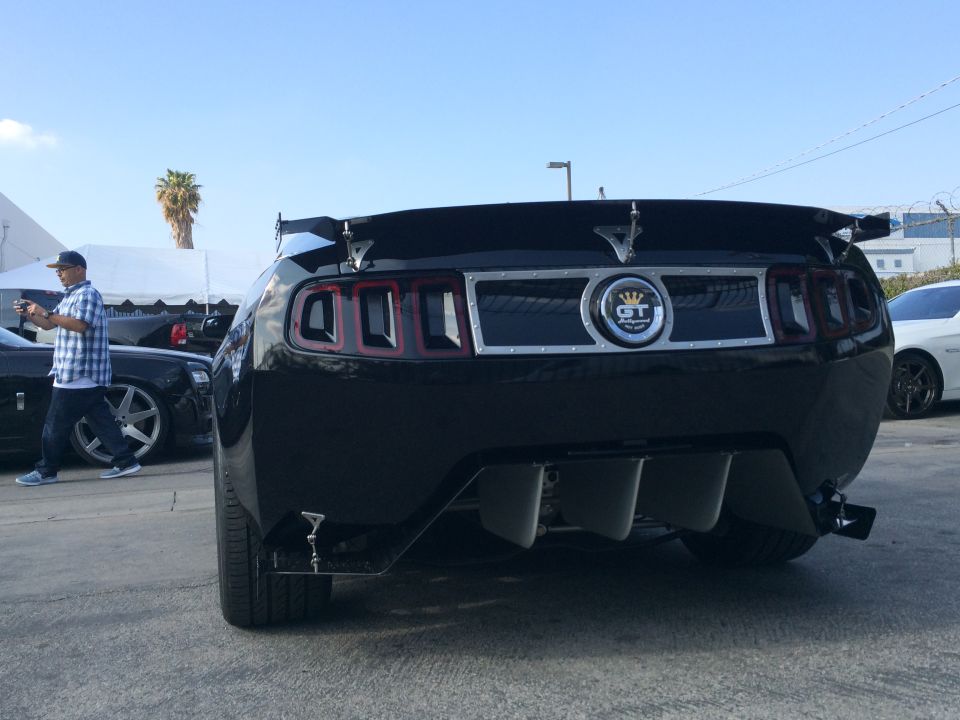 Black Ford Mustang with a rear spoiler and GT emblem, seen from the rear