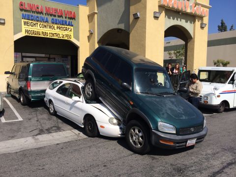 1968 Ford Mustang - A green SUV is parked on top of a white sedan, creating a bizarre scene in a parking lot.