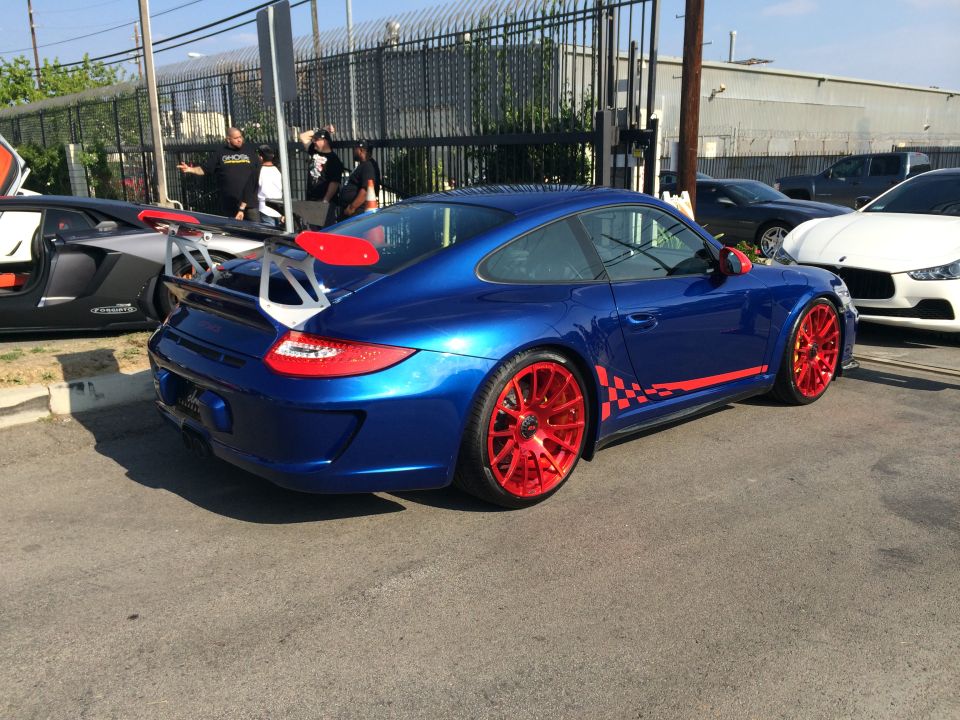 Blue Porsche 911 with red checkered stripe and red wheels, rear spoiler, parked on asphalt