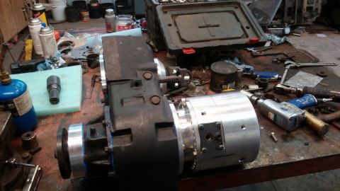 1995 Ford Bronco - A complex transfer case and auxiliary transmission assembly sits on a workbench, surrounded by tools and parts, suggesting a repair or modi…