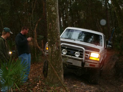 1991 Ford Bronco - A white 1991 Ford Bronco is seen navigating a muddy, wooded trail with two men observing.