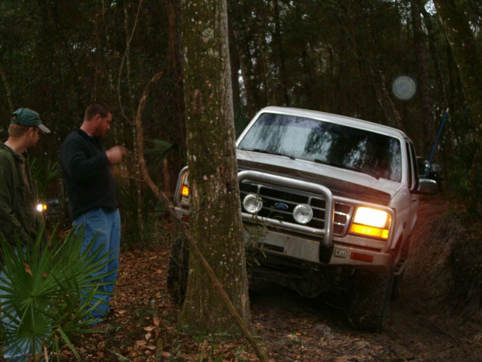White 1991 Ford Bronco with bull bar and off-road lights navigating a wooded trail