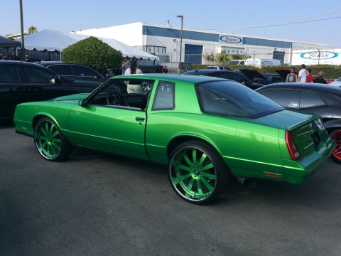 1968 Ford Mustang - A bright green coupe with large custom rims is parked outside a building with tents.