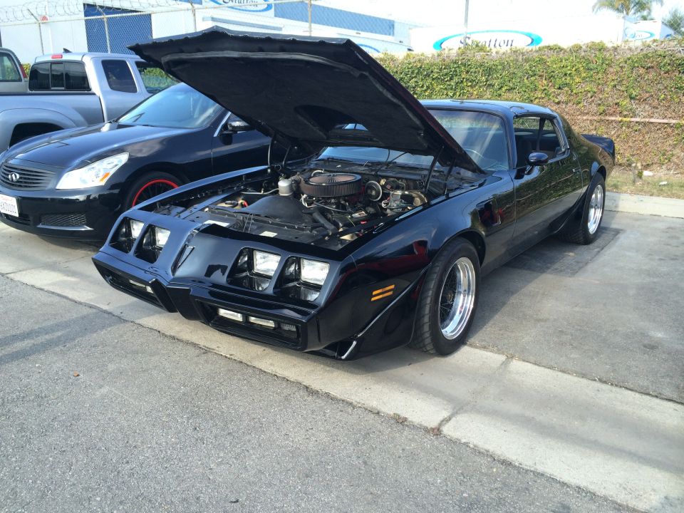 Black 1977 Pontiac Firebird Trans Am with hood open, showing engine