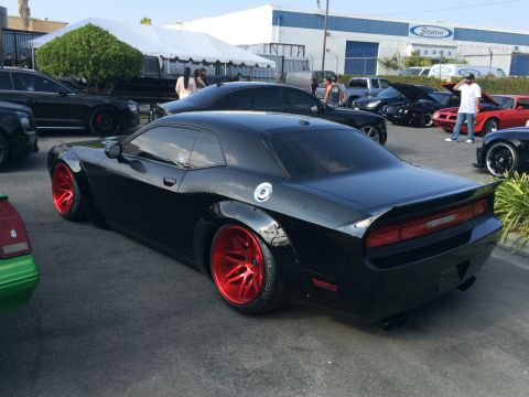 1968 Ford Mustang - Modified black Dodge Challenger with custom widebody and red wheels at an outdoor event.