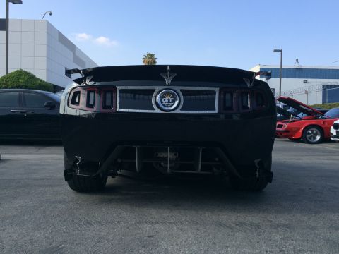 1968 Ford Mustang - A black car with a GT emblem and spoiler is parked outdoors.
