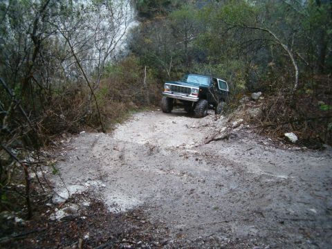 1991 Ford Bronco - A lifted dark green and white full-size Ford Bronco with a removable hardtop works down a rutted, rocky white-clay trail cut through dense…