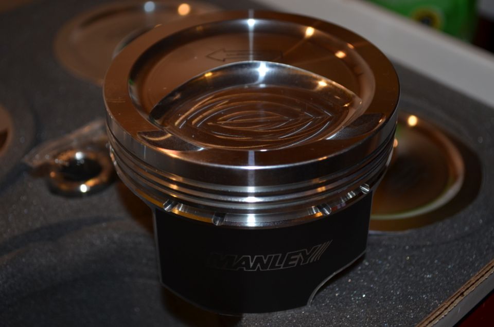 Manley piston with engraved logo and machined top surface, resting on dark foam padding