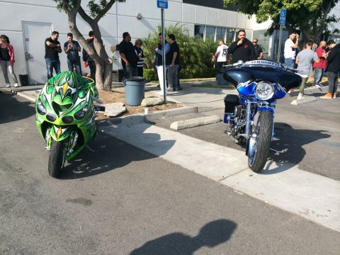 1968 Ford Mustang - Two custom motorcycles, one green sportbike and one blue cruiser, are parked outside a building with people gathered around.