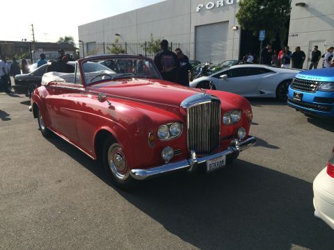 1968 Ford Mustang - A red Bentley convertible is parked in front of a building with other cars around it.