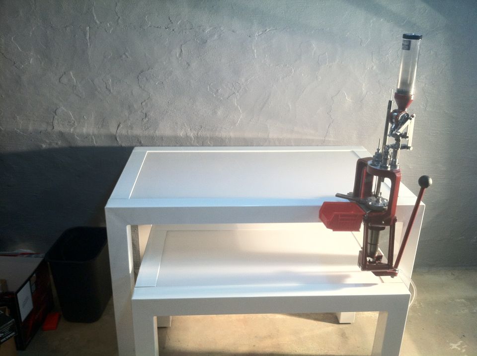 Red reloading press with a clear powder hopper mounted on a white table
