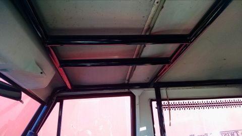 1985 Jeep CJ7 - Interior view of a vehicle's roof showing a black metal roll cage with red accents, trim pieces. Pinkish light filters through the windows.