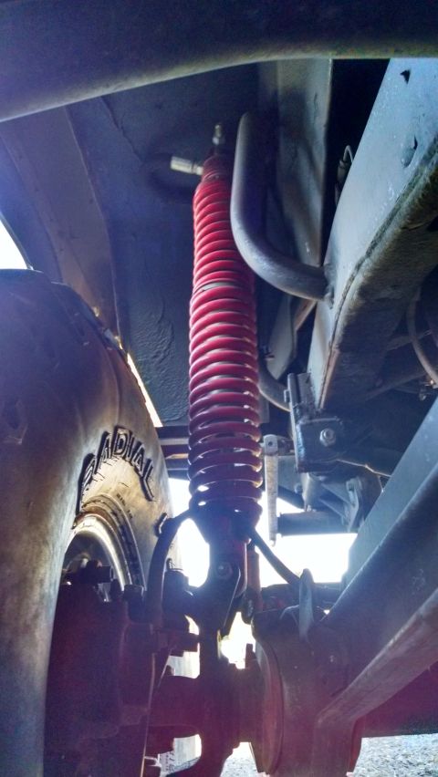 1985 Jeep CJ7 - Close-up view of a red coilover shock absorber and part of a tire, likely from a Jeep CJ7.