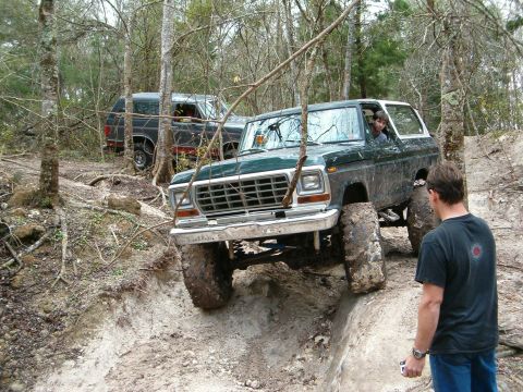 1991 Ford Bronco - Two Ford Broncos navigate a challenging off-road trail in a wooded area.