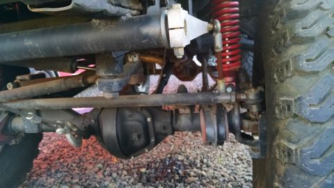 1985 Jeep CJ7 - Close-up view of front axle and suspension components, including a red coilover shock absorber.