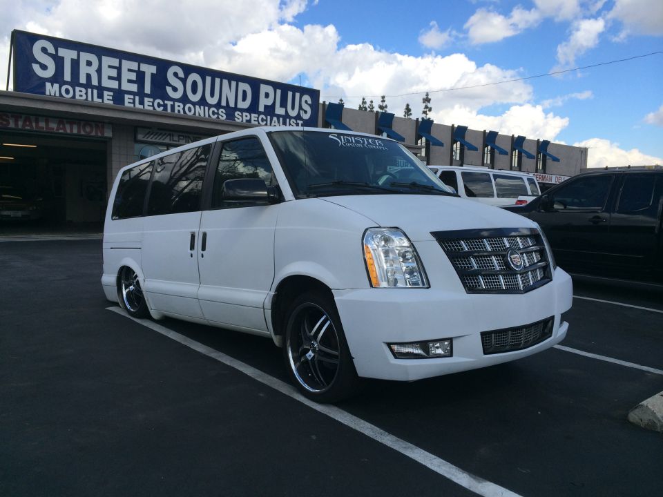 White van with a Cadillac Escalade front end conversion parked in a lot. "Street Sound Plus" sign above