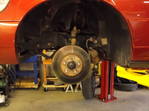1999 Mercury Grand Marquis - Front wheel assembly and suspension of a red vehicle undergoing service, with the Supermotors.net logo visible at the bottom.