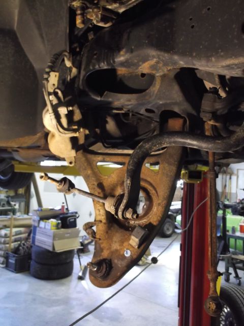 1999 Mercury Grand Marquis - Close-up view of heavily rusted front suspension parts on a vehicle undergoing repairs.