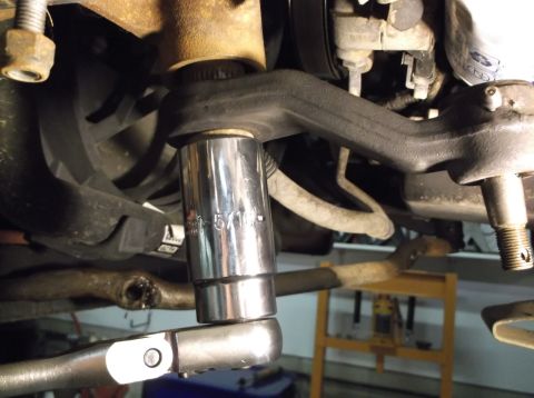 1999 Mercury Grand Marquis - Mechanic using a socket wrench on a vehicle's suspension system component.