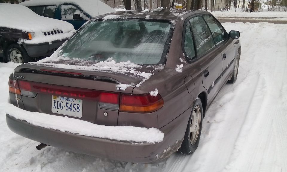 1996 Subaru Legacy sedan parked in snow, rear 3/4 view. Another vehicle is partially visible to the left