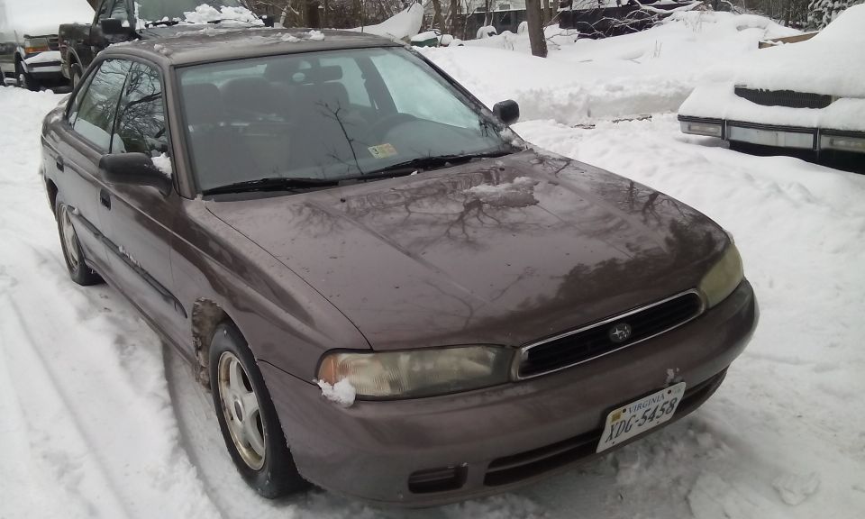 1996 Subaru Legacy sedan parked in snow, front passenger side view. Another vehicle is partially visible in the background