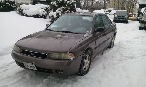 1996 Subaru Legacy - A 1996 Subaru Legacy sedan sits in a snowy driveway with other vehicles nearby.