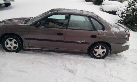 1996 Subaru Legacy - A brown sedan sits in a snowy environment, partially covered by snow.